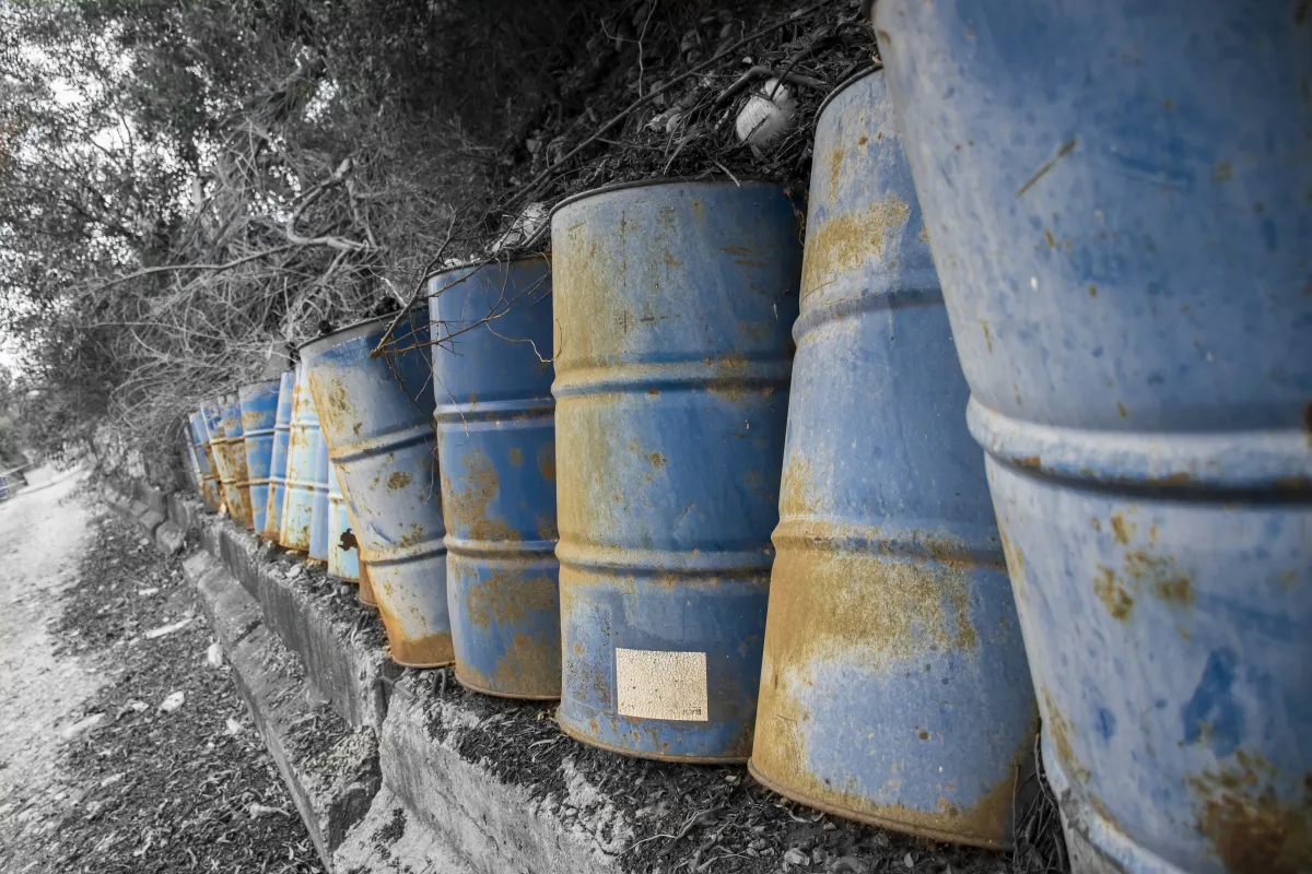 Row of weathered blue barrels leaning along an earthen slope in selective color